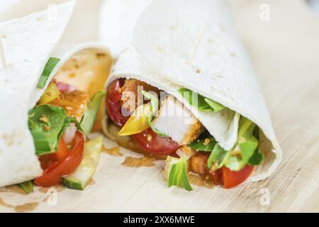 Wrap di pollo (primo piano dettagliato, messa a fuoco selettiva) su sfondo in legno Foto Stock