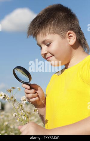 Il ragazzo vede i fiori attraverso la lente d'ingrandimento Foto Stock