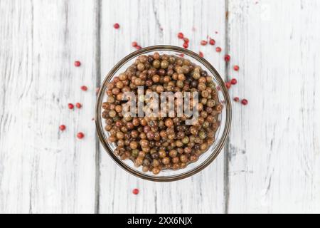 Grani di pepe rosa freschi (conservati) su un vecchio e rustico tavolo in legno, messa a fuoco selettiva, foto ravvicinata Foto Stock