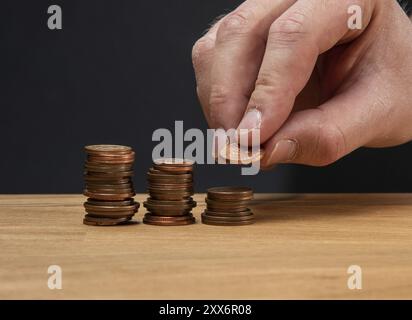 Una mano che impilava monete su un tavolo di legno su uno sfondo scuro Foto Stock