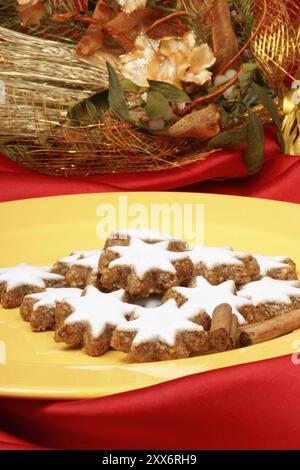 Primo piano di alcuni biscotti alla cannella (in tedesco Zimtsterne) sono tipici biscotti natalizi tedeschi e svizzeri su piatto giallo su sfondo rosso Foto Stock