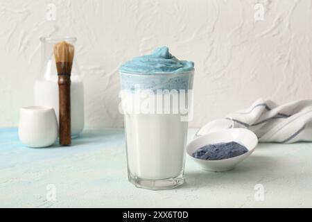 Bicchiere di latte matcha dalgona blu, tovagliolo e ciotola con matcha in polvere su un tavolo leggero Foto Stock