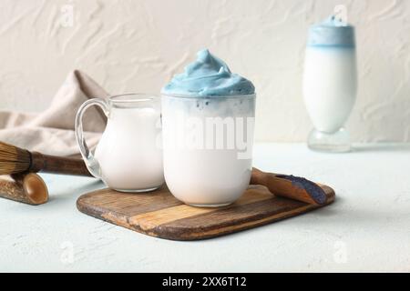 Bicchiere di latte matcha dalgona blu, caraffa di latte e vassoio di legno su un tavolo leggero Foto Stock