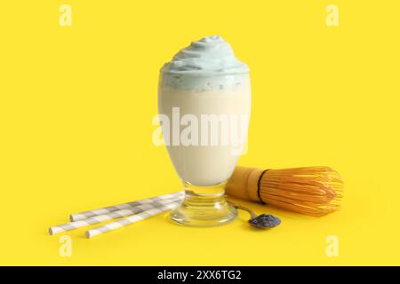 Bicchiere di dalgona blu matcha latte, cannucce, chasen e cucchiaio su sfondo giallo Foto Stock