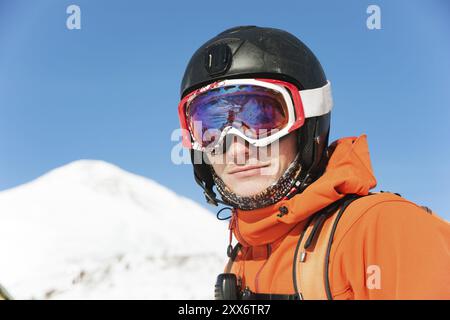 Ritratto di uno sciatore in una tuta arancione con uno zaino sulla schiena in un casco si staglia sullo sfondo di una splendida terra di montagna caucasica Foto Stock