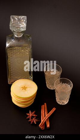 Liquore di mele con spezie su sfondo nero, alcol fatto in casa in vetro di cristallo, cannella e anice. Primo piano. Foto Stock