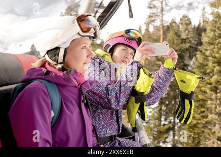 Le donne che praticano lo snowboard hanno fotografato al telefono mentre sono sedute nella cabina di risalita Foto Stock