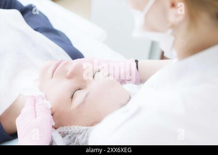 Un primo piano della procedura di pulizia nell'ufficio di cosmetologia. Le mani del cosmetologo in guanti rosa sono rimosse dal viso di un giovane Foto Stock