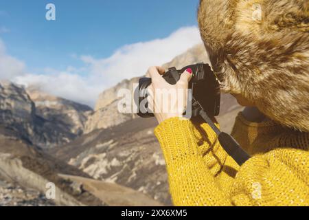 Fotografa turistica con cappello di pelliccia e maglione giallo in montagna scatta foto con la sua fotocamera digitale. Il concetto di fotografia in viaggio Foto Stock