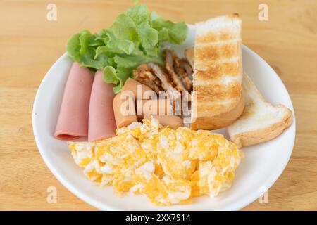 Un delizioso piatto da colazione con uova strapazzate, affettati, pane tostato e verdure fresche per un inizio sano. Foto Stock