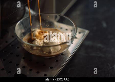 Caffè versato da una macchina per il caffè sul gelato in un contenitore di vetro. Foto Stock