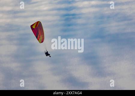 Un parapendio rosso e giallo vola sopra uno strato di nuvole bianche in un cielo azzurro. Foto Stock