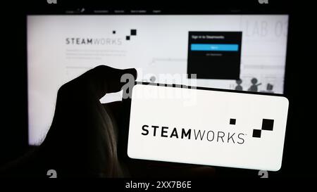 Persona che possiede lo smartphone con il logo dell'interfaccia di programmazione dell'applicazione Steamworks (Steam) davanti al sito Web. Mettere a fuoco il display del telefono. Foto Stock