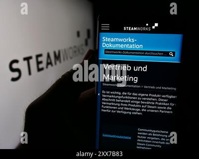 Persona che tiene un cellulare con la pagina Web dell'interfaccia di programmazione dell'applicazione Steamworks (Steam) davanti al logo. Messa a fuoco al centro del display del telefono. Foto Stock