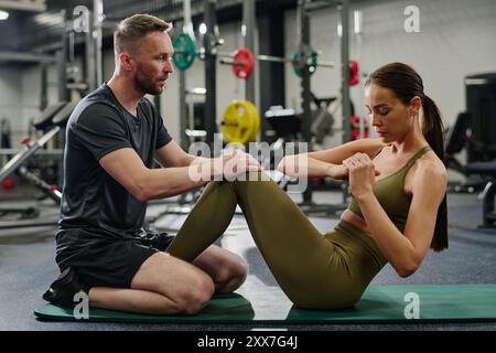 Personal trainer che aiuta il suo atleta a far oscillare la pressa nella palestra vuota Foto Stock