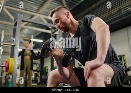 Tiro ad angolo basso di un uomo che fa esercizio bicipite mentre il suo amico si prepara a fare gli squat Foto Stock