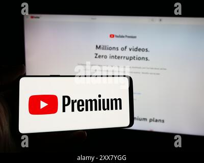 Persona con smartphone con logo del servizio di abbonamento streaming video YouTube Premium davanti al sito Web. Mettere a fuoco il display del telefono. Foto Stock