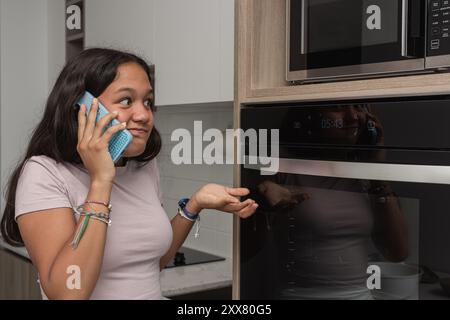 Adolescente che chiama per telefono per chiedere aiuto per cucinare. Foto Stock