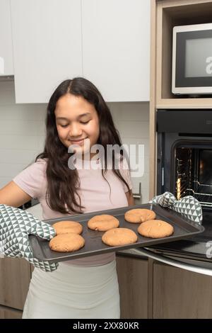 Ragazza felice che mostra i suoi biscotti appena sfornati a casa Foto Stock