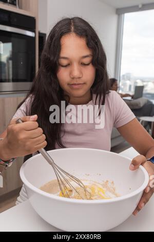 Una ragazzina a casa mescola gli ingredienti in un recipiente grande. Foto Stock