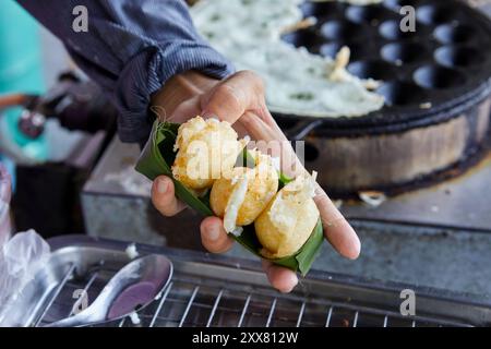 Mano tagliata che tiene le torte di cocco-riso in un recipiente con foglie di banana Foto Stock