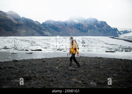 Giovane uomo in giacca gialla cammina vicino al ghiacciaio in Islanda Foto Stock