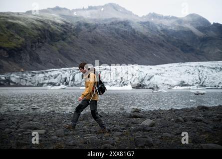 Giovane uomo in giacca gialla cammina vicino al ghiacciaio in Islanda Foto Stock