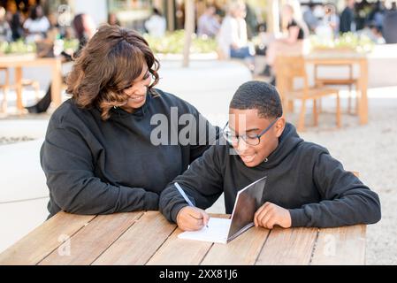 Bambino che scrive nel suo taccuino con zia che aiuta Foto Stock