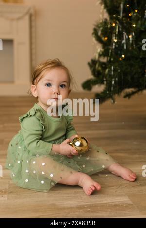 Bambina in abito verde davanti all'albero di natale Foto Stock