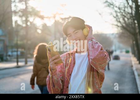 Allegro felice giovane asiatico di 20 anni indossa la camicia ascoltare la musica con le cuffie Foto Stock