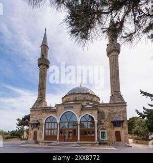 La Moschea Sehitler, o Moschea dei Martiri a Baku, Azerbaigian, presenta due alti minareti e una facciata ornata, circondata da alberi sullo sfondo di nuvole Foto Stock