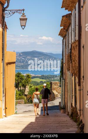 Francia, Var, Gassin, etichettato come i più bei villaggi della Francia, coppia di turisti in un vicolo del villaggio con il Golfo di Saint-Tropez sullo sfondo Foto Stock