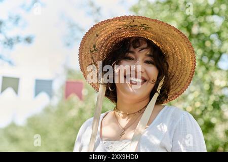 Una giovane donna con un cappello di paglia sorride brillantemente in un lussureggiante giardino estivo. Foto Stock