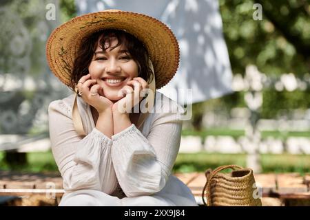 Una giovane donna con un cappello di paglia e una camicetta bianca sorride radiosamente in un giardino estivo. Foto Stock