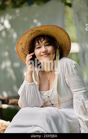 Una donna bruna sorride dolcemente mentre indossa un cappello di paglia e una camicetta bianca in un giardino. Foto Stock