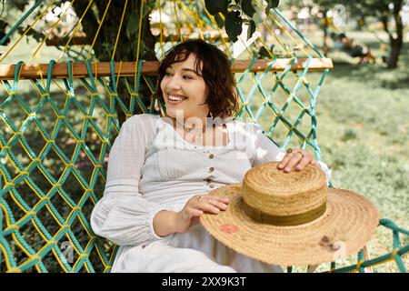 Una giovane donna con un abito bianco e un cappello di paglia si rilassa su un'amaca in una soleggiata giornata estiva. Foto Stock