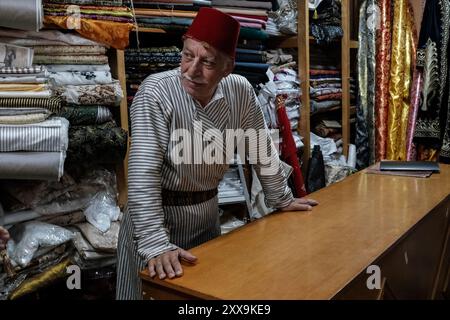 Il commerciante tessile di Gerusalemme Bilal Abu Khalaf si trova nel suo negozio nel quartiere cristiano della città Vecchia, circondato da tessuti che mostrano quello della sua famiglia Foto Stock