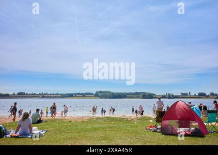 Turisti sulla spiaggia artificiale interna sulla riva del lago artificiale di Rutland, in Inghilterra, durante le vacanze scolastiche estive del 2024. Foto Stock