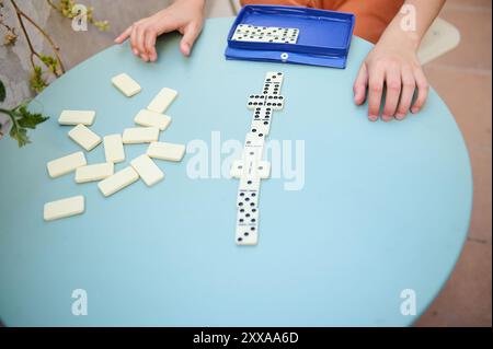 Mani che giocano a domino su un tavolo blu. Le piastrelle sparse suggeriscono un'atmosfera coinvolgente e divertente. Foto Stock