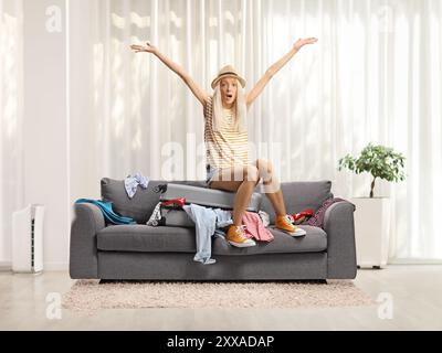 Una giovane donna sorprende seduta su una valigia su un divano di casa Foto Stock