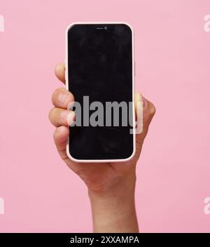 Una persona ha in mano un iPhone nero con uno sfondo rosa. Il telefono non è acceso e la persona lo sta tenendo vicino alla fotocamera. Concetto di distacco Foto Stock