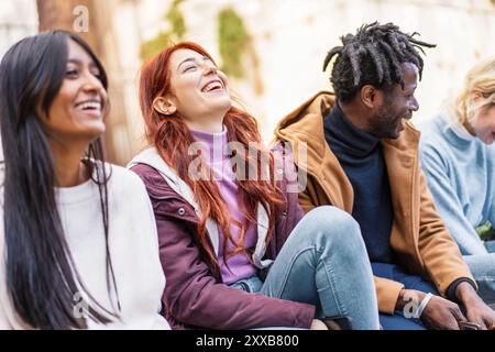 Gioioso gruppo multiculturale di giovani adulti che ridono insieme in un ambiente urbano. Autentici momenti di felicità tra amici diversi, in mostra incl Foto Stock