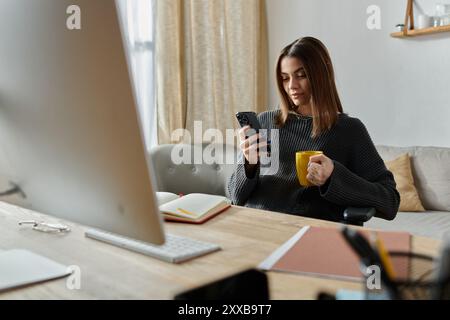 Una donna lavora da casa, incollata al telefono, sorseggiando un caffè, probabilmente gestendo il marketing digitale. Foto Stock