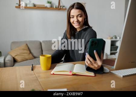 Una giovane donna lavora in remoto da casa, sorridendo mentre usa il telefono per creare contenuti. Foto Stock