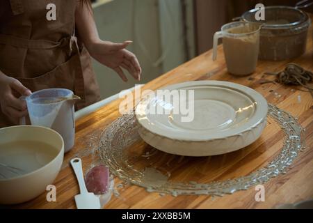 Primo piano di una donna ceramista che crea un piatto di ceramica dall'argilla in officina Foto Stock