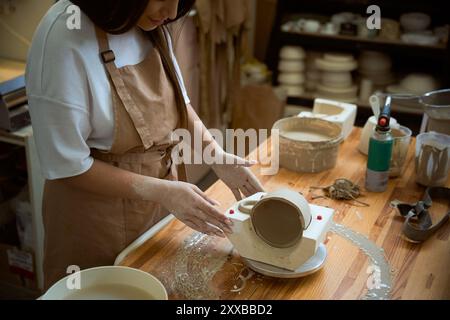 Tavolo in studio di ceramica con artista che forma l'argilla bagnata per la tazza di vasaio Foto Stock