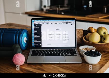 Laptop con ChatGPT aperto sul bancone della cucina con frutta, spuntini e attrezzature per l'allenamento, stile di vita sano, lavoro remoto, vita equilibrata, fitness a. Foto Stock