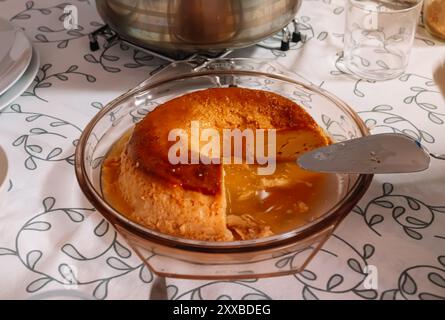 Flan tagliato a pezzi in un recipiente con la spatola per distribuire porzioni sul tavolo della sala da pranzo. Foto Stock