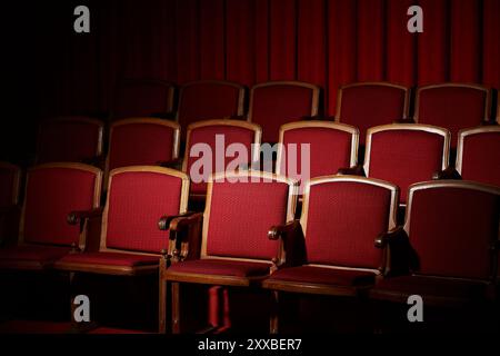 File di posti vuoti in velluto rosso in un cinema buio, l'attesa rimane nell'aria. Foto Stock