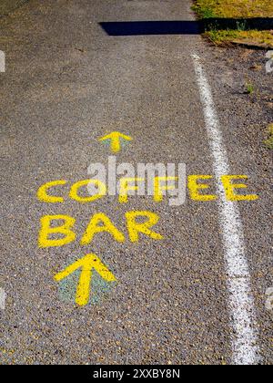 Testo giallo brillante "COFFEE BAR" con frecce dipinte su asfalto, parte della segnaletica stradale del cammino di Santiago. Foto Stock